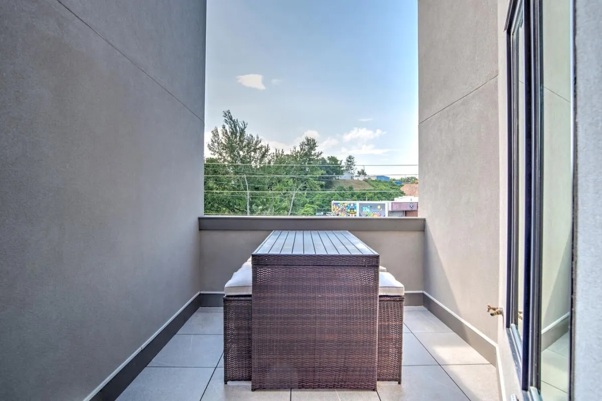 An exterior patio scene with an outdoor dining table set against a backdrop of lush green trees and an open sky. The serene atmosphere hints at the elevated, private nature of the outdoor space, perfect for dining or enjoying the sunset above the city.
