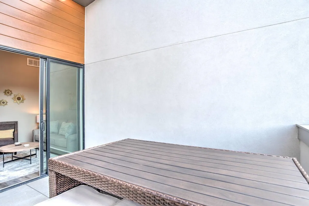A well-lit area featuring a wooden dining table set near a glass door, with a cozy couch in the background and decorative wall art. The setup suggests a seamless transition from indoor socializing to enjoying outdoor views, underlining the living space’s versatility.