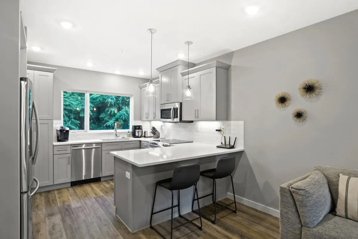 A modern kitchen featuring a central island, stainless steel appliances, large window with a city view, and decorative wall art. The space is bathed in warm, natural light, making it both functional and welcoming for cooking, entertaining, and socializing.