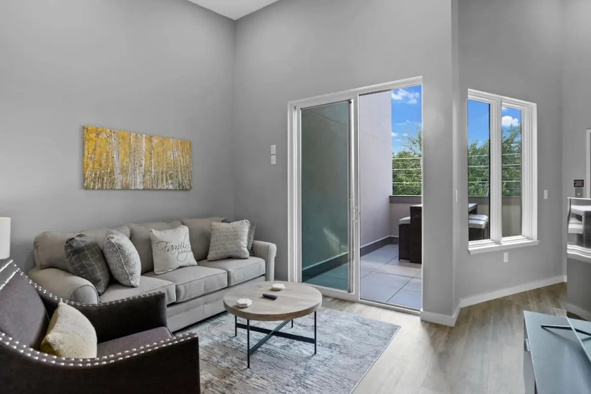 This image captures a cozy sitting area featuring a sofa and coffee table, with direct access to a balcony offering expansive views. The space is filled with natural light, suggesting a perfect spot for morning coffee or evening relaxation while gazing at the skyline.