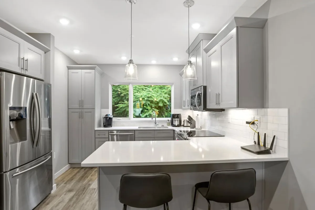 A modern kitchen featuring a spacious island, sleek stainless steel appliances, and a large window that brings in natural light and a view of lush greenery. The layout suggests a versatile space suitable for both casual dining and focused work sessions, with ample room for socializing or enjoying a quiet moment with morning coffee.